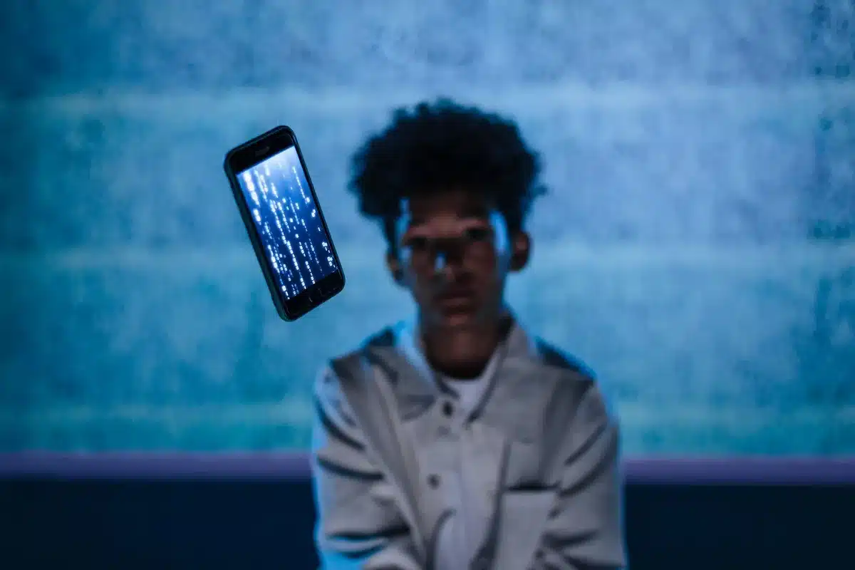 A silhouette of a young person gazing at a glowing smartphone screen in a dimly lit room, their face illuminated by the device's light, symbolizing the isolation and dependency risks of AI companionship