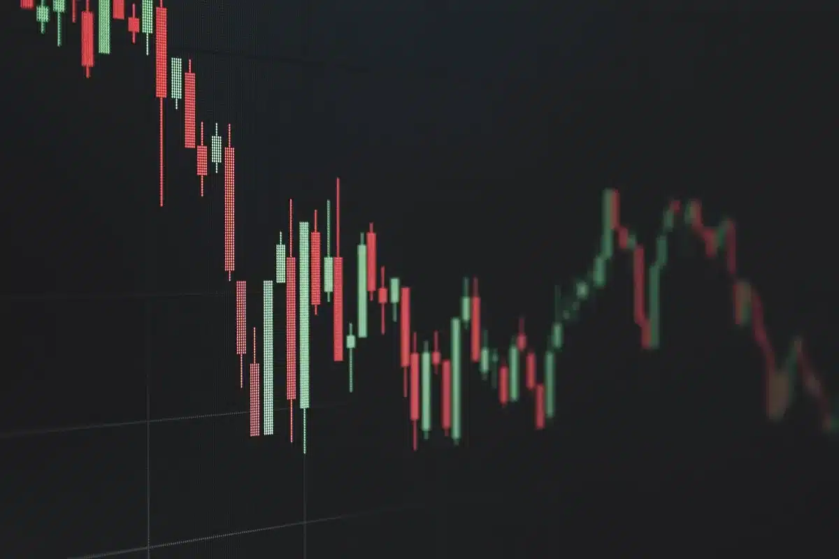 A glowing cryptocurrency exchange chart on a dark screen, candlestick lines trending downward, blurred trading indicators in the background, anonymous trader silhouette in dim light