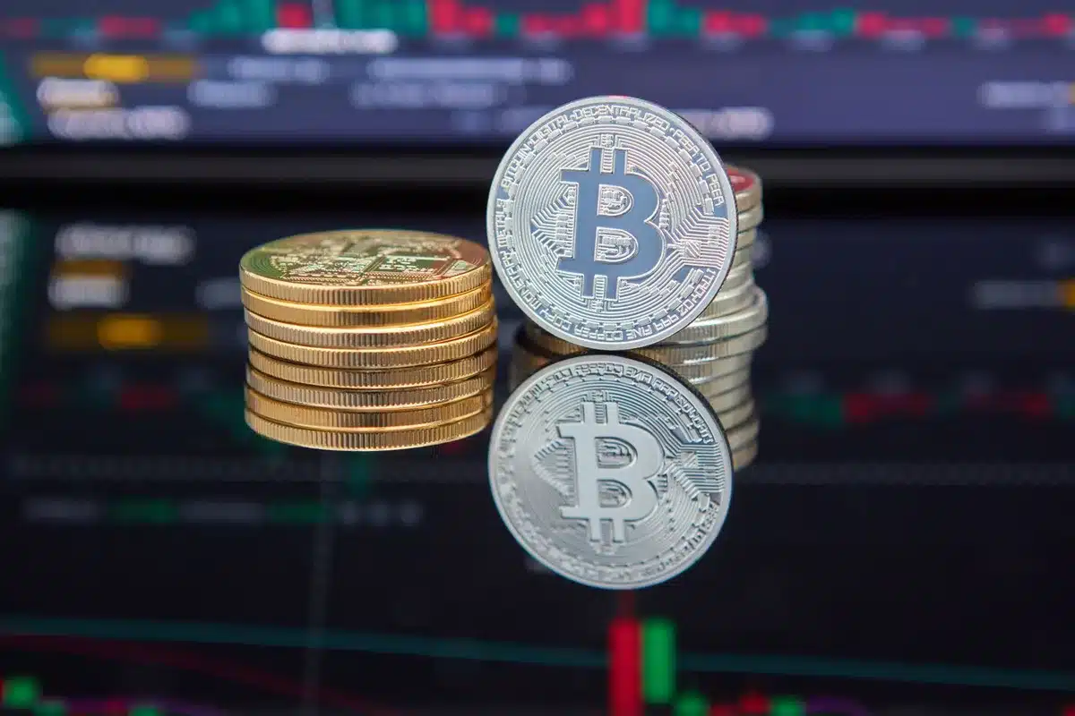 A crowded trading floor with multiple screens showing Bitcoin ticker symbols and upward arrows, traders reacting with raised arms and focused expressions, blue and green lighting reflecting off glass panels