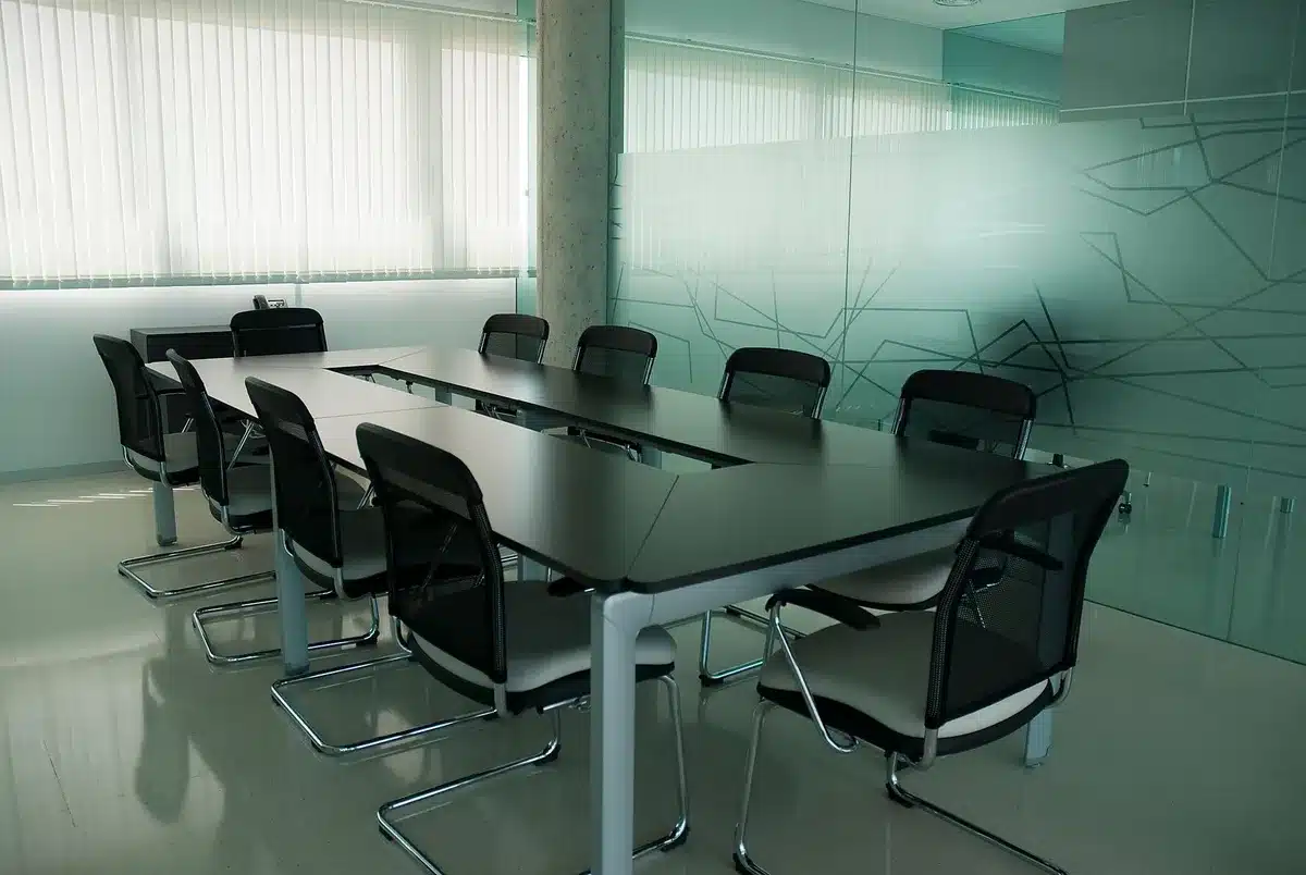 A formal government building's modern conference room with a long table, multiple empty chairs, notepads, and water glasses arranged for a high-level meeting, soft natural light streaming through tall windows, anticipatory atmosphere.