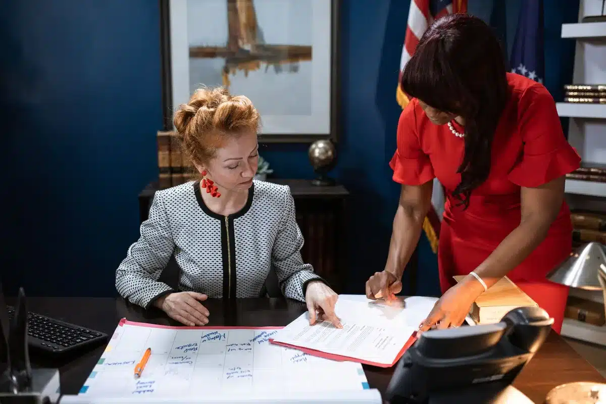 A congressional office corridor with tall windows, an empty desk visible through an open door, a nameplate stand ready to be engraved, formal marble and wood interior, soft natural light.