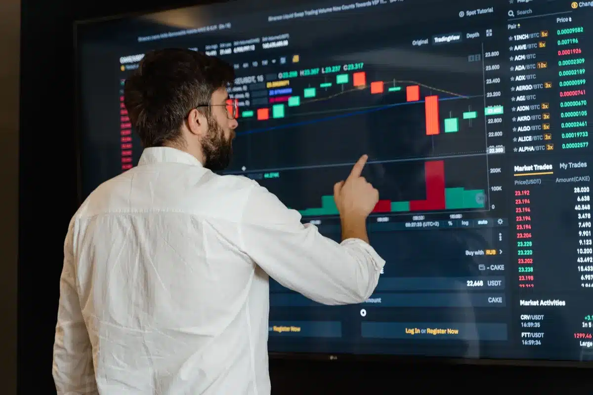 Stock market trading floor with multiple screens displaying pharmaceutical stock tickers and price charts in real-time, traders monitoring data, green and red numbers reflecting market movement