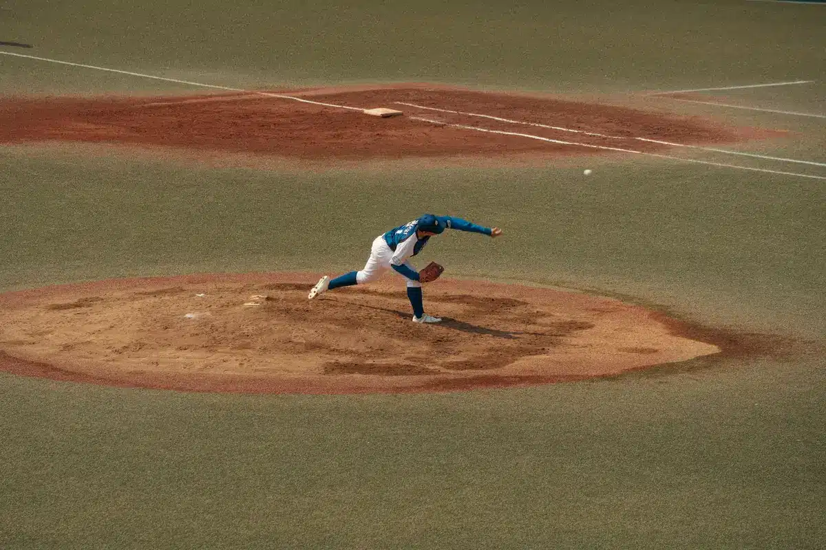 A pitcher in mid-delivery on the mound, arm extended upward, focused expression, stadium crowd blurred in background, stadium lights reflecting off the field, moment of release captured