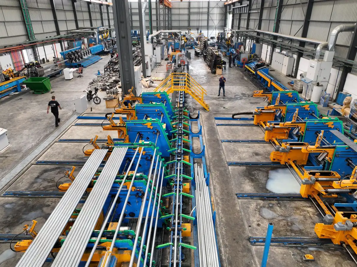 An aircraft manufacturing facility interior with a partially assembled fuselage section under bright industrial lighting, technicians in yellow safety vests working at stations, rivets and structural framework visible, conveying precision assembly