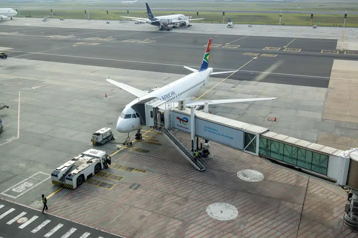 Construction site preparation at a major airport, concrete foundations and temporary structures, heavy equipment staged, blue sky, modern urban infrastructure in background