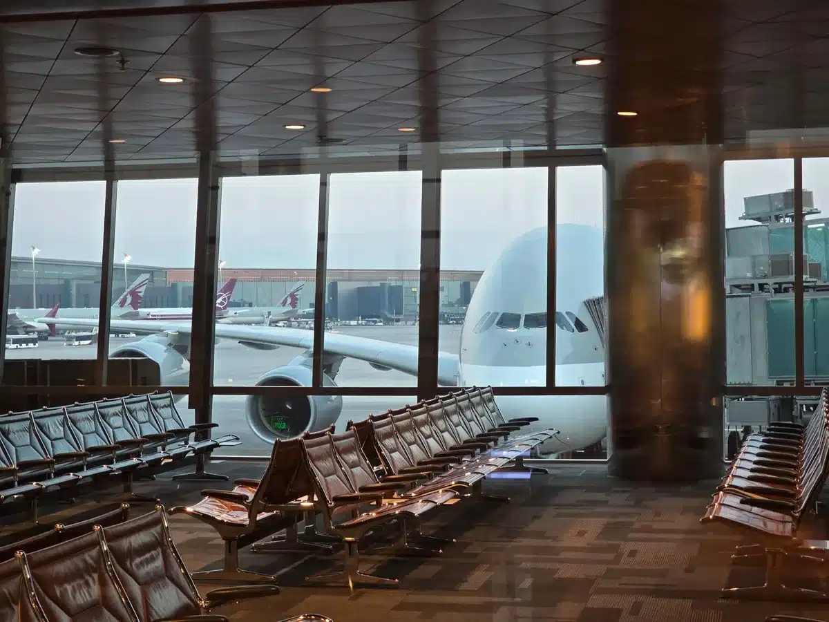 A commercial airport gate area with empty seating and departure boards displaying route information, suggesting a period of reduced flight operations