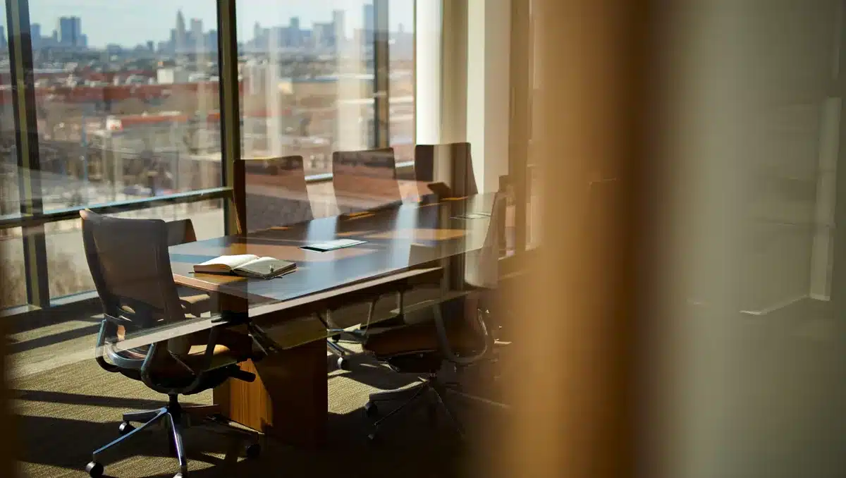 A modern foundation office with glass walls overlooking a city skyline, empty chairs around a polished conference table awaiting trustees, morning light streaming through floor-to-ceiling windows, a single notebook open on the table &mdash; succession.