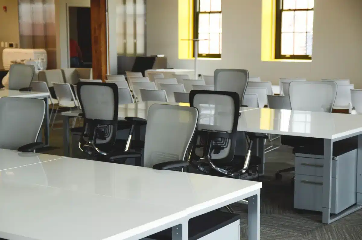 An empty government office with desks abandoned, chairs pushed back, and personal items removed, sunlight streaming through windows, evoking mass departure and institutional exodus.
