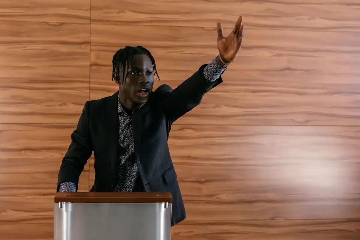 A split-screen comparison showing a podium on one side with a microphone and empty chair, and on the other side a closed door or darkened space, representing the contrast between public defense and absence