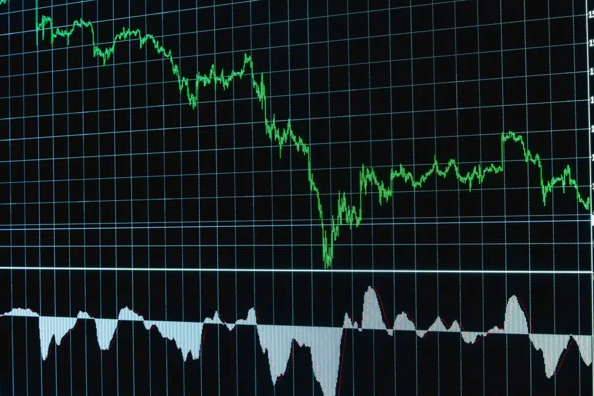 Empty trading floor with dimmed screens reflecting red market losses, a single workstation illuminated with upward-trending charts, solitary conviction amid broader market decline
