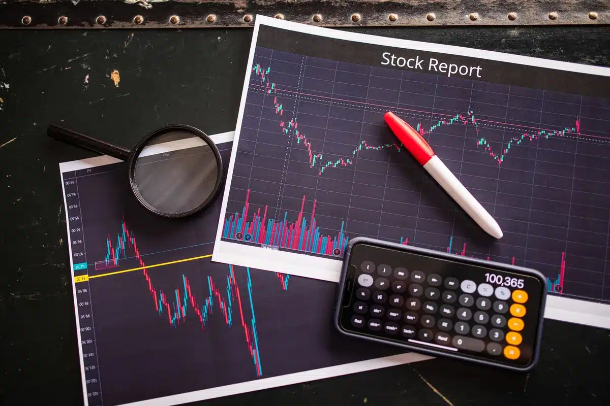 Professional woman reviewing financial documents and data on a desk with laptop and charts, hands visible examining stock portfolio information.