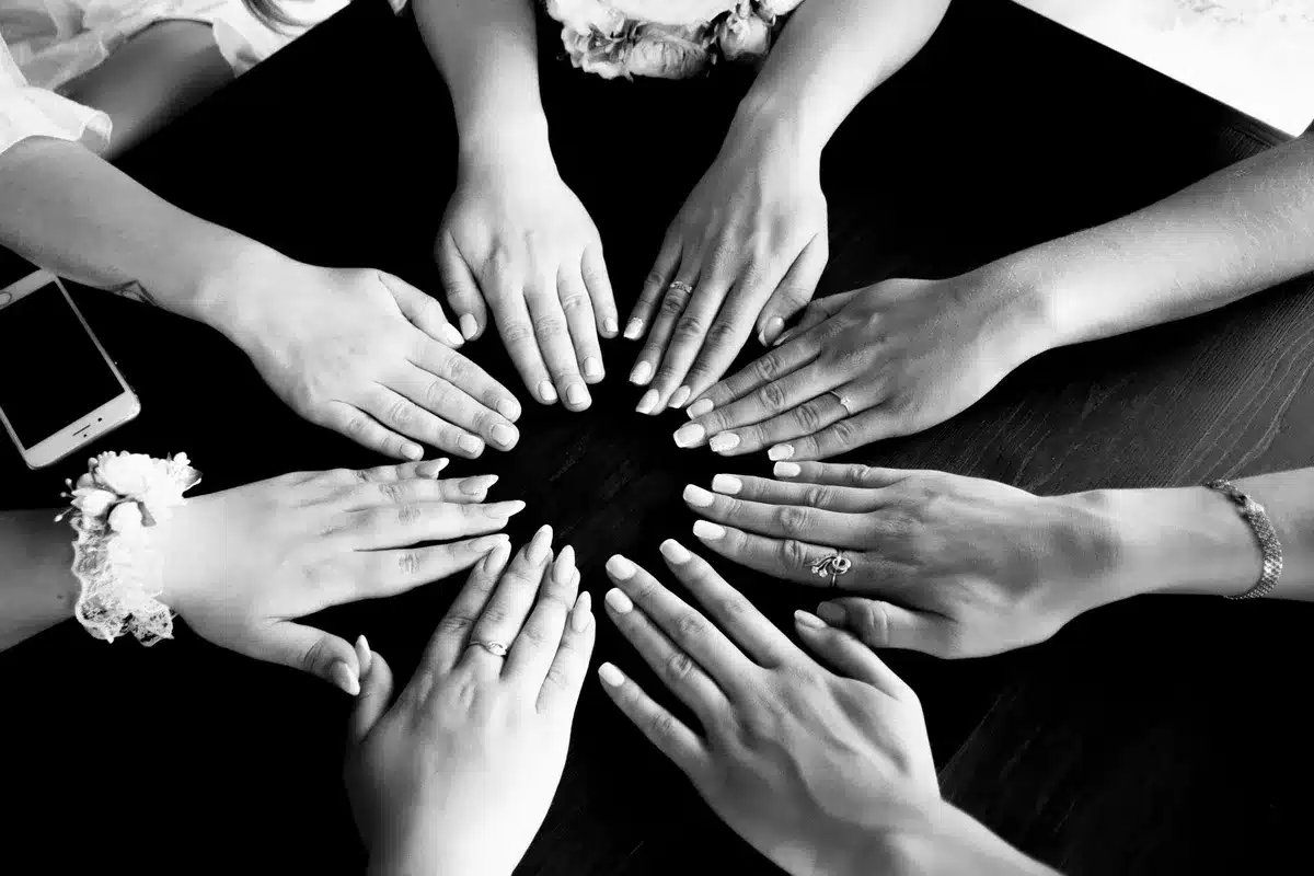 A diverse group of hands joined together in a circle viewed from above, symbolizing unity and inclusion, against a neutral background