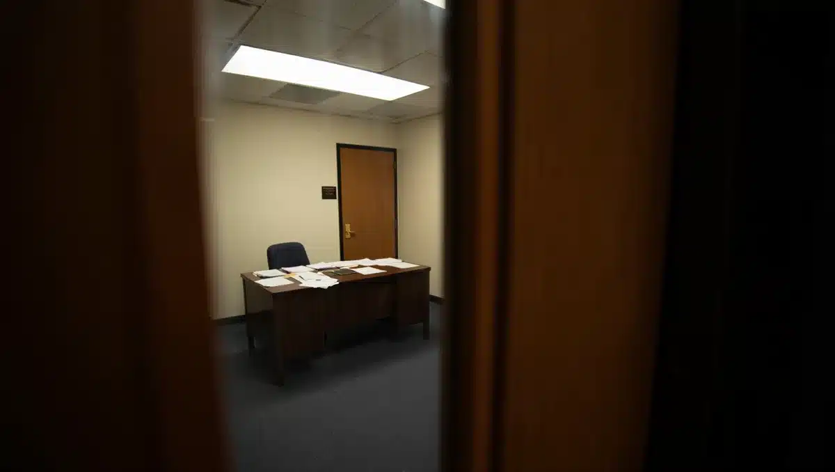 Congressional office with empty desk and closed door, harsh fluorescent lighting, abandoned workspace suggesting sudden departure, tension.