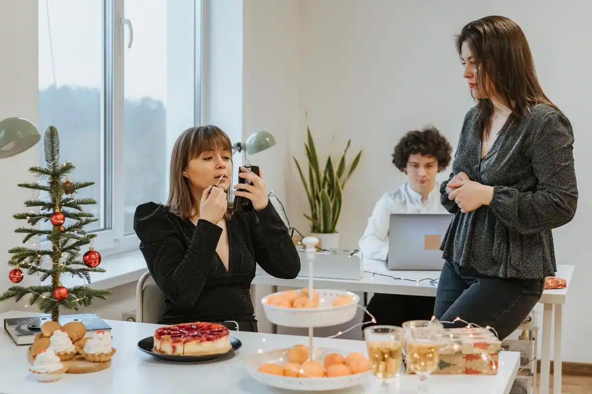 Two young female office workers at desks with uncomfortable body language, surrounded by gift boxes and luxury items, one woman looking away with a strained expression, fluorescent office lighting, tension visible — discomfort