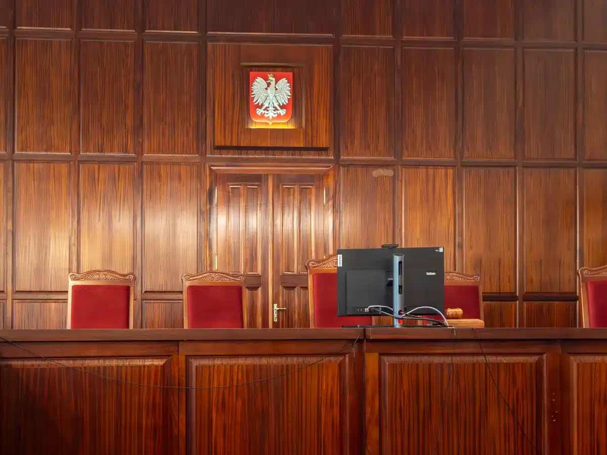 Empty House chamber floor with a single podium under harsh overhead lights, rows of vacant seats stretching into shadow, the chamber feeling solemn and formal — accountability