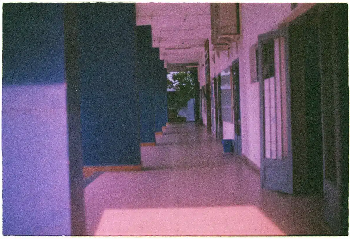 Congressional staff members walking a hallway lined with office doors, fluorescent light overhead, documents in hand, serious expressions, the machinery of legislative negotiation