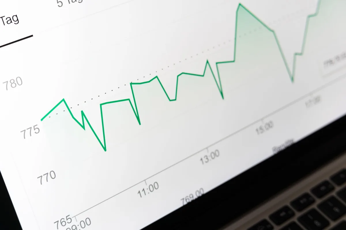 A glowing stock ticker screen in a dim trading floor, numbers scrolling upward and downward, a silhouette of a trader's hand reaching toward the display, long-term investment thesis visualized