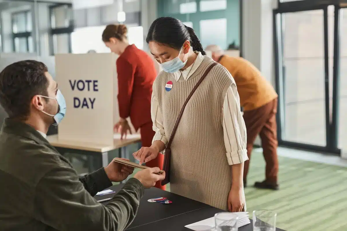 Early voting location with anonymous citizens casting ballots in individual booths marked with American flags, soft overhead lighting, a sense of civic participation
