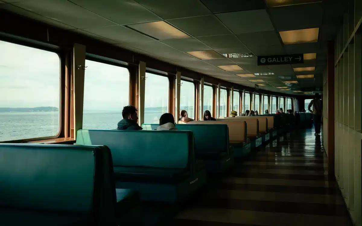 Two cruise ship passengers in a heated confrontation in a narrow corridor, one recording on a phone, the other gesturing aggressively, cabin doors visible in the background.