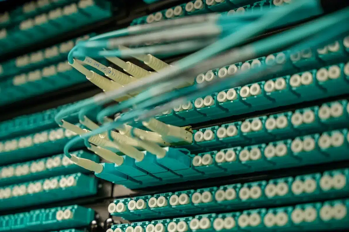 Glowing server racks and GPU hardware in a data center, blue and white light casting across rows of computing equipment, condensation visible on cooling systems, the scale and density of infrastructure stretching into shadow