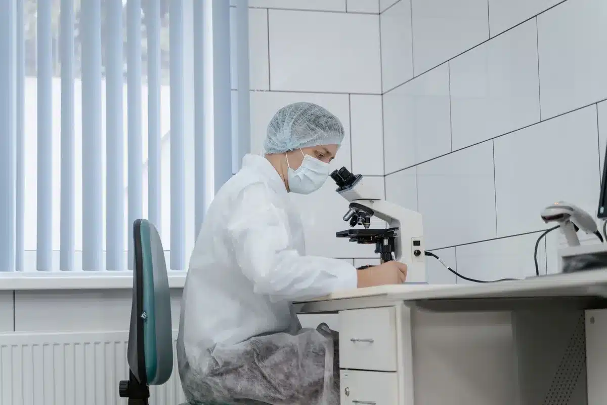 Laboratory technician examining microscope slides with parasite samples, clinical setting with test tubes and medical equipment, precise scientific work in progress