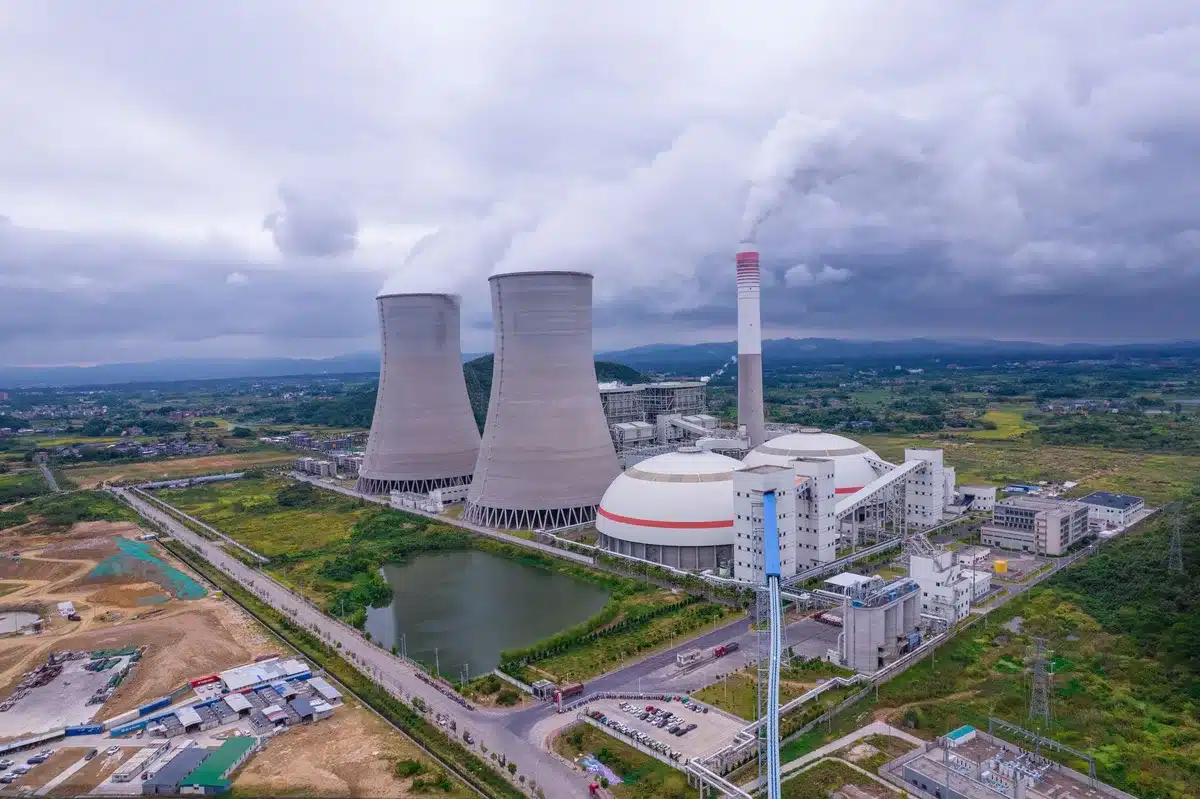 Sprawling power plant facility beside a nearly empty riverbed, cooling towers reflected in shallow water, industrial infrastructure amid drought conditions