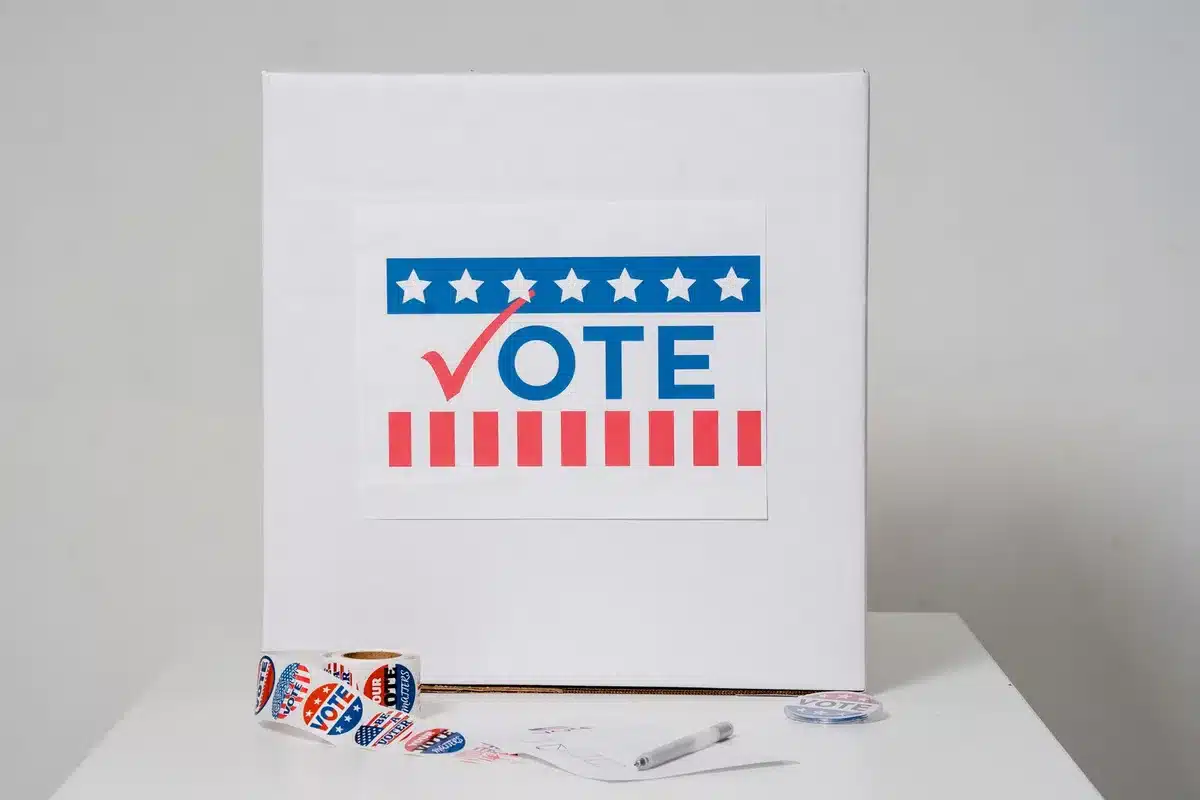 An empty podium with microphones on a stage, soft spotlight illuminating the space, a voting booth visible in the background shadow, American flags flanking the sides, anticipation in the stillness