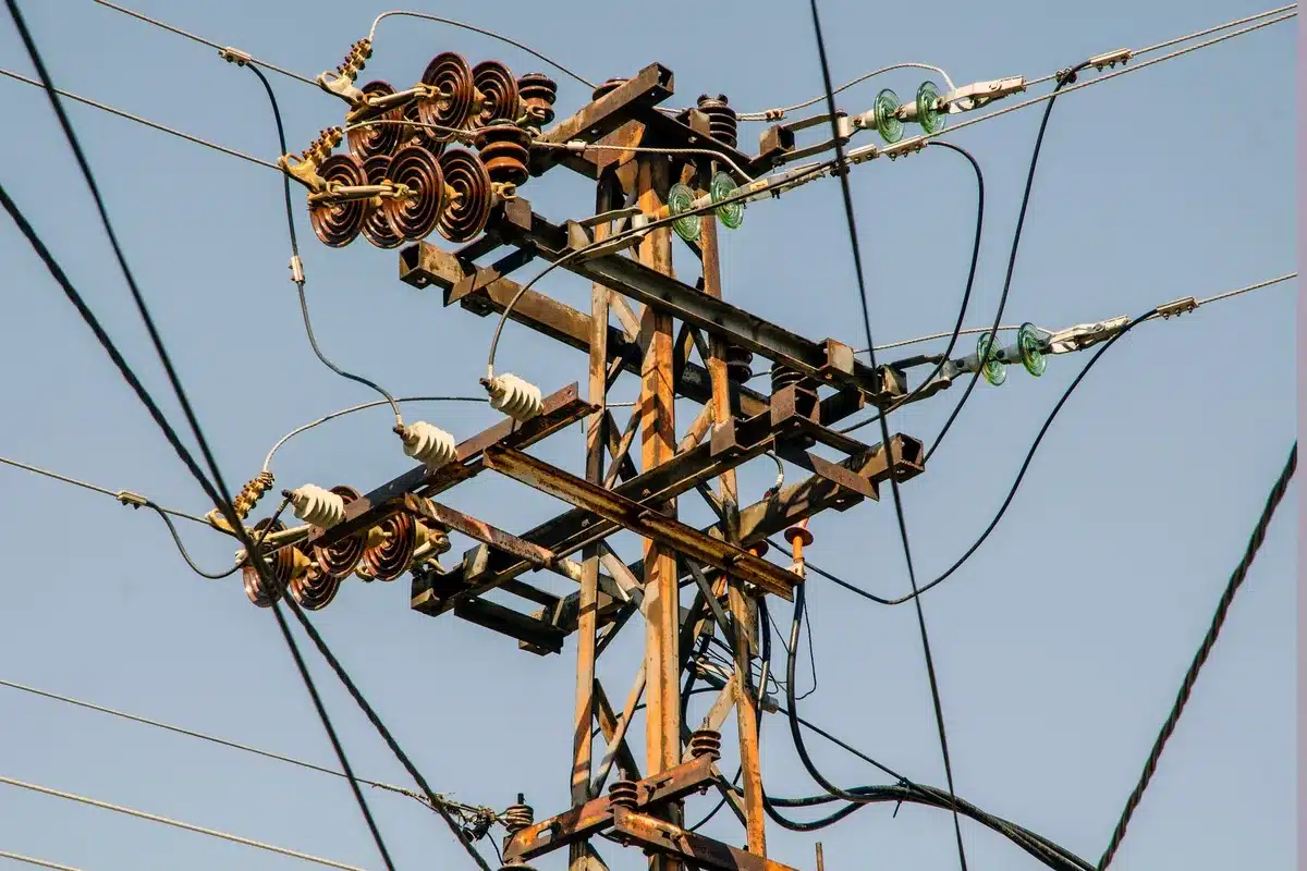 A split-screen showing a glowing electrical grid map on the left with red stress indicators, and empty transmission tower silhouettes against a sunset on the right, representing grid strain