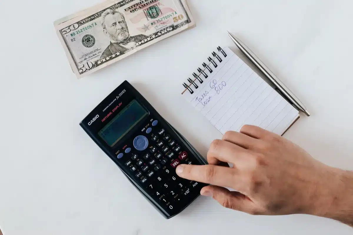 A person sitting at a desk reviewing budget documents and financial statements, with a calculator and notepad visible, afternoon natural light streaming through a window