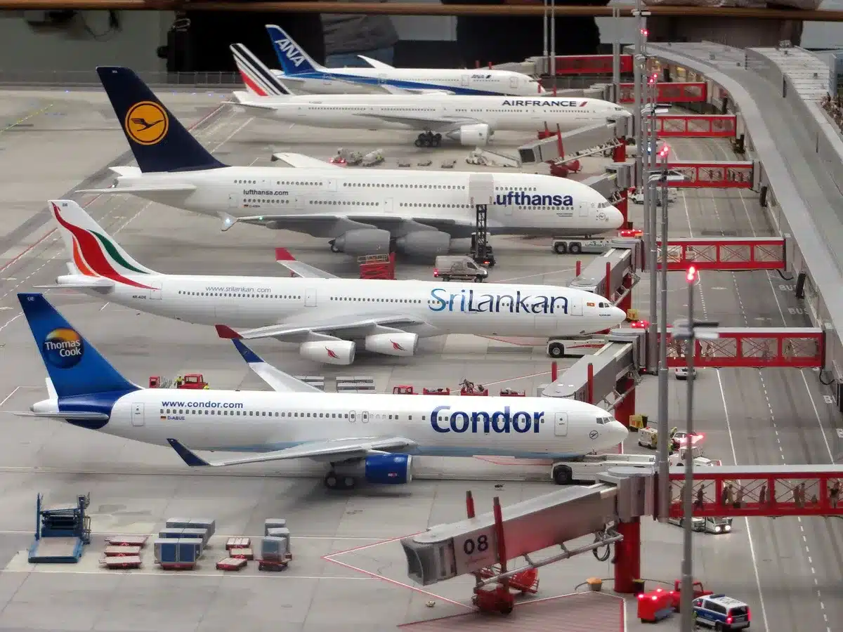 Airport taxiway at dawn, emergency evacuation slides deployed from aircraft fuselage, passengers walking on tarmac with ground vehicles in background, emergency lights visible