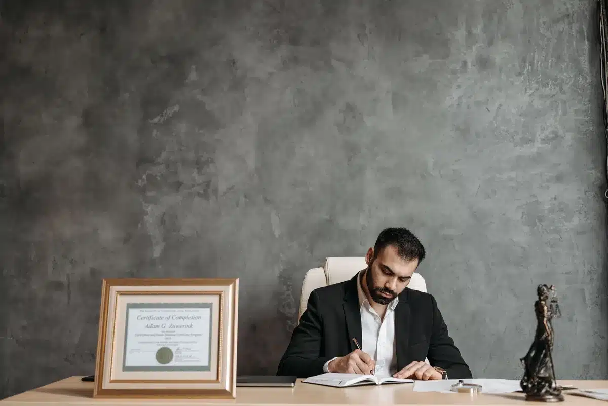 A dimly lit office or study space with law books on shelves, a desk with scattered papers, and a single desk lamp casting focused light, evoking isolation and professional distance