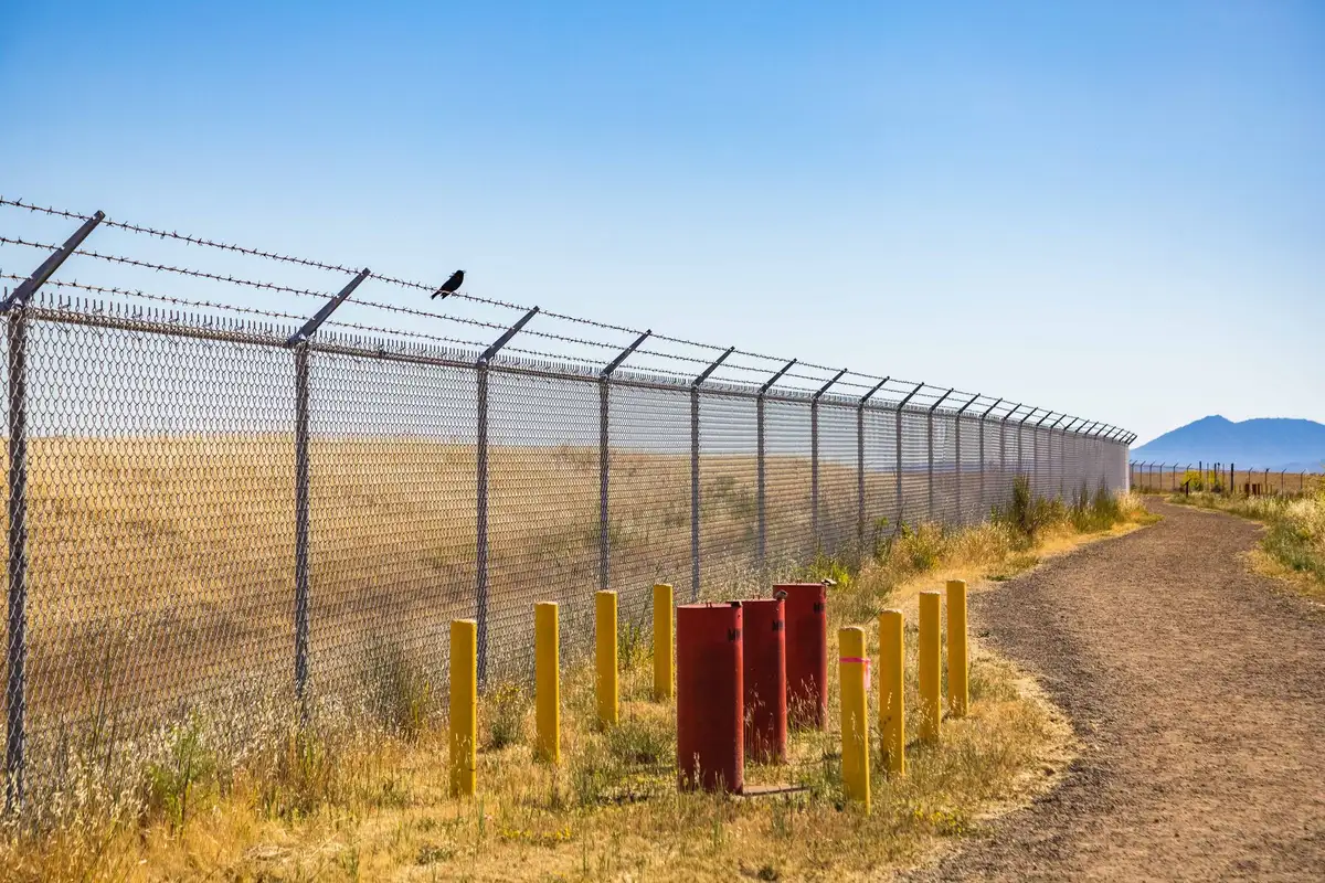 DHS Secretary and border officials standing at the Rio Grande border wall section, examining construction and security infrastructure with CBP Commissioner beside them