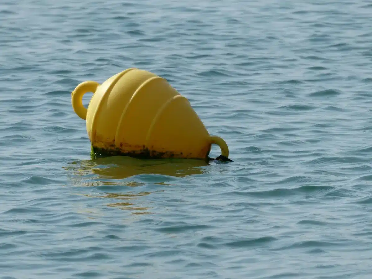 Floating orange and white buoy barriers stretching across the Rio Grande River, with the far bank visible in soft daylight, water rippling around the structures