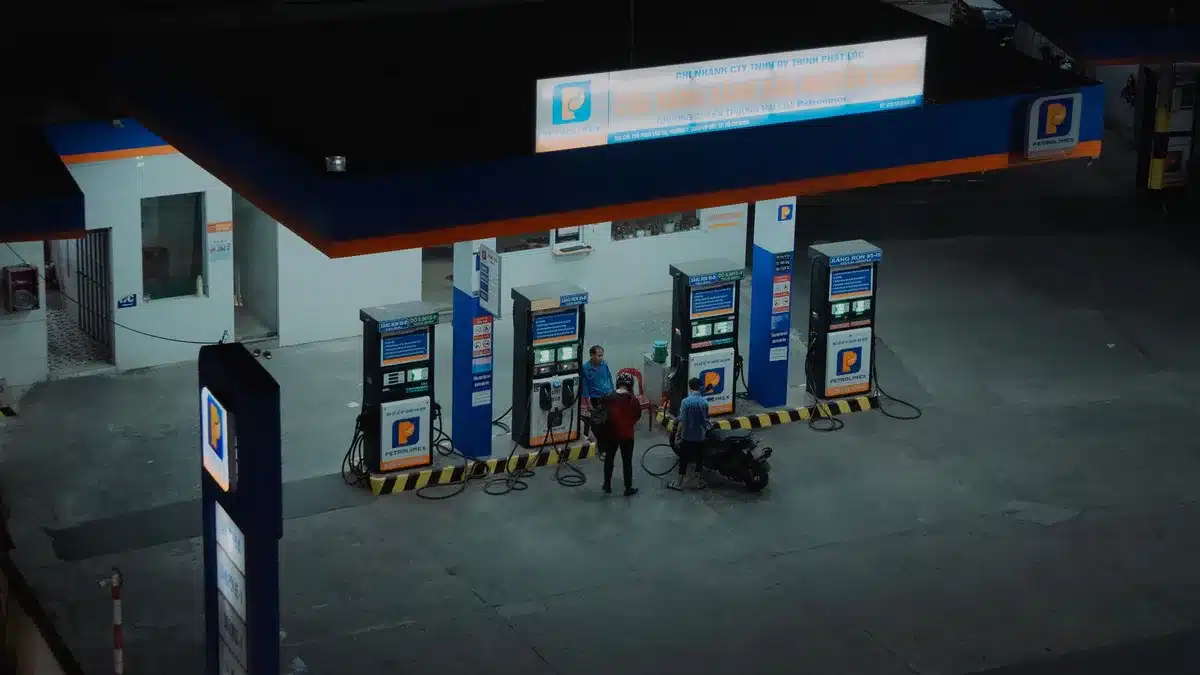 Fuel pump nozzle at a gas station displaying high prices on a digital display, close-up macro shot of numbers changing, bright daylight illuminating the screen