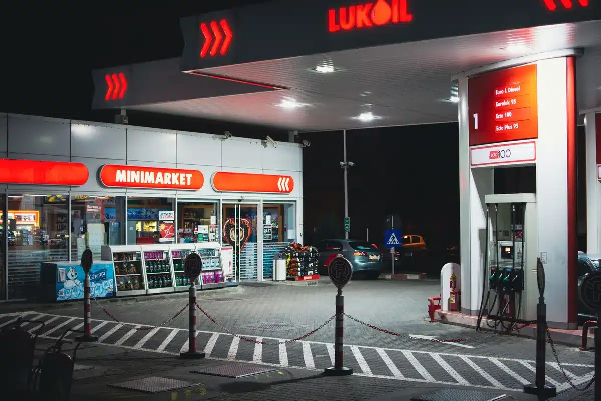 Fuel pump display showing diesel price at record high, bright red numbers glowing against dark background, gas station canopy overhead, a hand reaching toward the pump handle