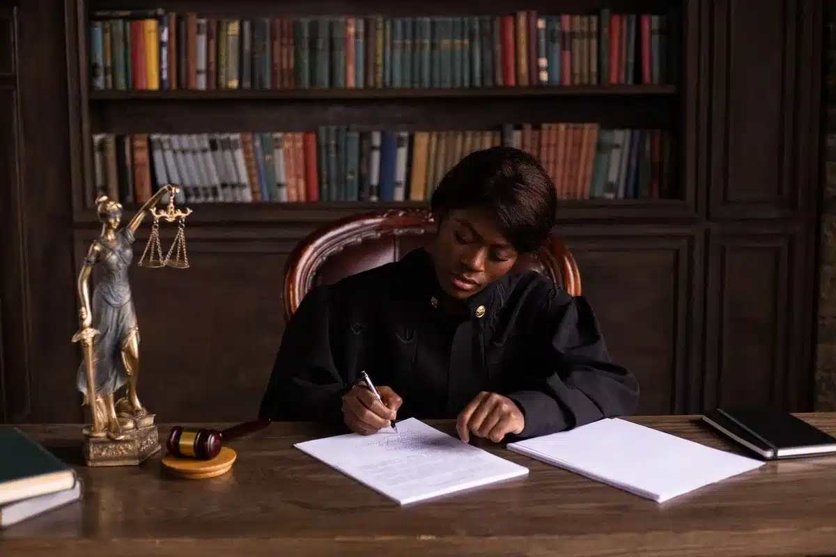 A law office desk with scattered case files and a framed victim support certificate, soft natural light from a window, suggesting quiet legal advocacy work