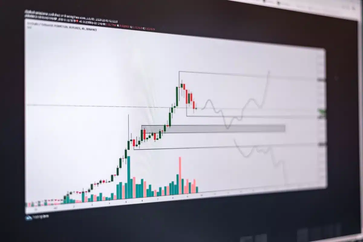 A stock market ticker display showing red numbers and declining price charts, candlestick graphs trending downward, a digital screen bathed in red light reflecting trader concern, muted color palette emphasizing loss.