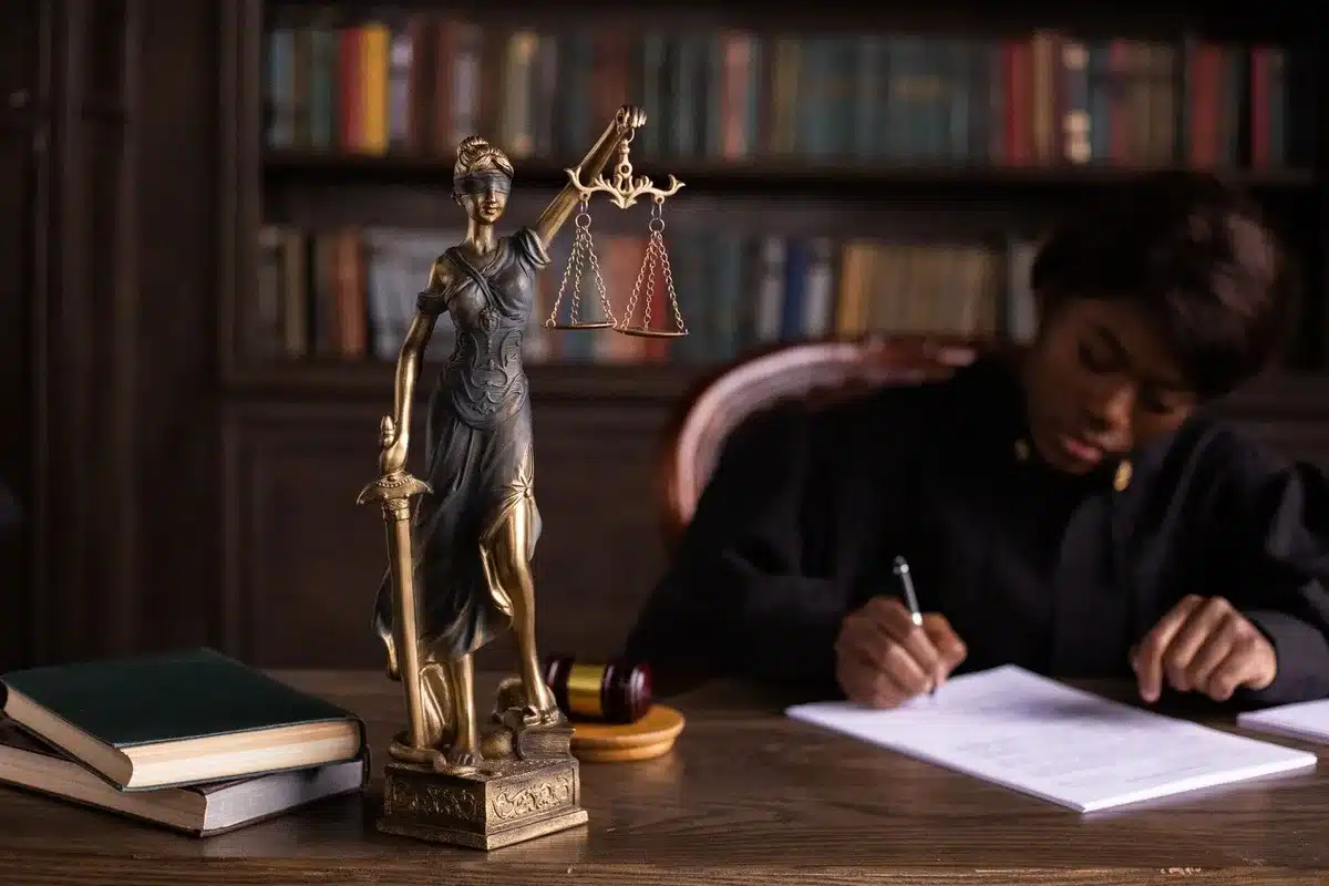 A gavel resting on a desk in a dim courtroom, with law books and papers blurred in the background, scales of justice visible nearby
