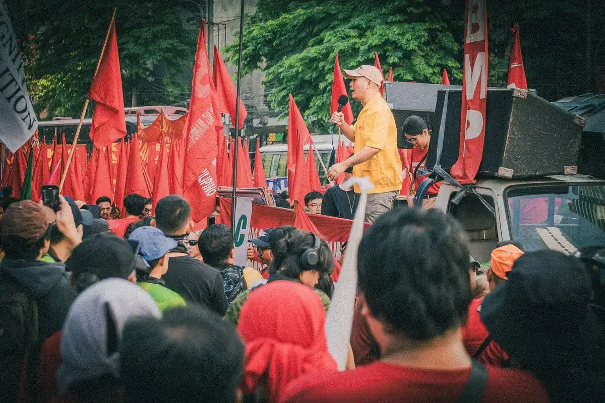 A crowded convention hall filled with young activists holding socialist banners and signs, faces animated in discussion and celebration, bright overhead lighting casting sharp shadows on the crowd