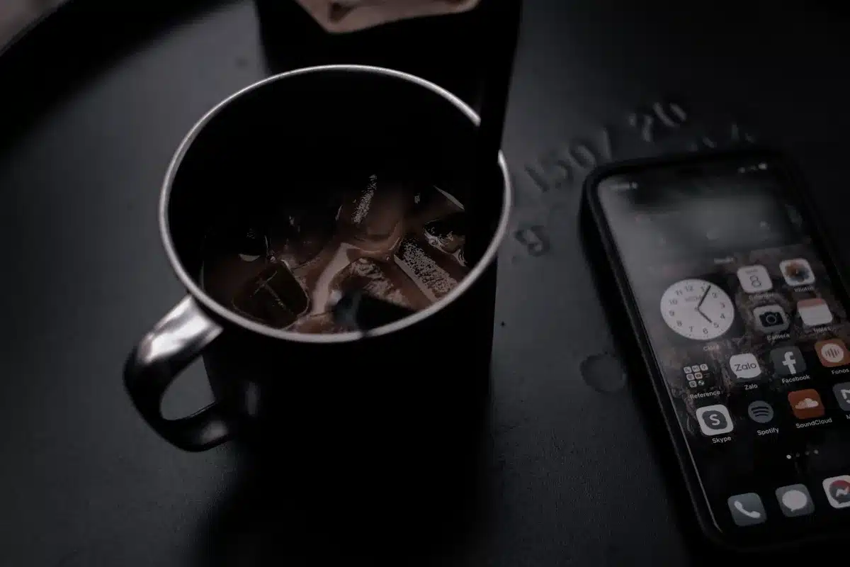 A tall iced coffee with condensation beading on the glass, ice cubes visible, sitting on a bright surface with the Dunkin' app visible in the background