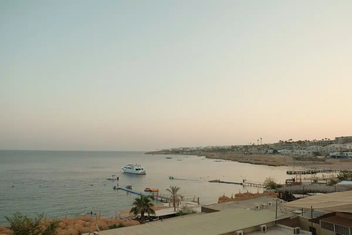 An aerial view of Hurghada's Red Sea coastline with resort buildings and calm turquoise waters, showing the coastal development along the rift zone, with distant desert hills visible