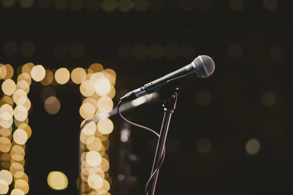 A microphone under a single spotlight in a dark studio, dust particles drifting through the beam, symbolizing divisive rhetoric