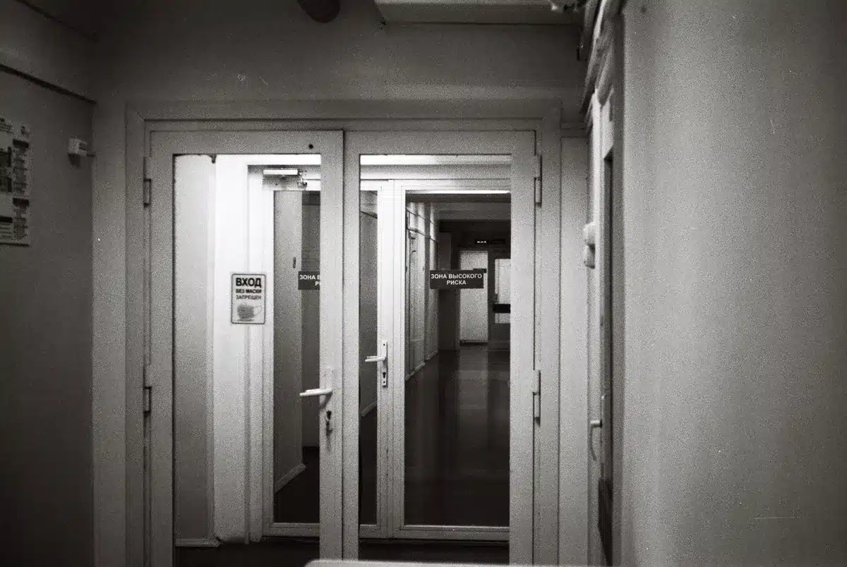 A closed door in a dim hallway with harsh light casting sharp shadows, representing political distance