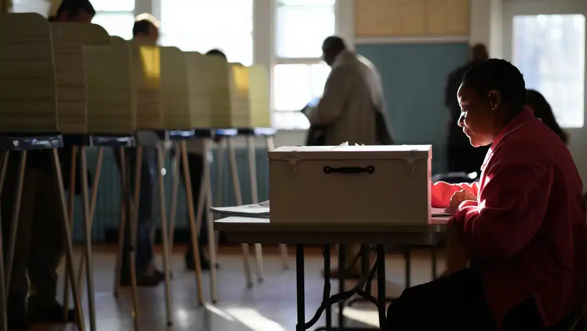 Polling place interior with voting booths, ballot box, and election workers checking in voters, midday light through windows | voting location primary election