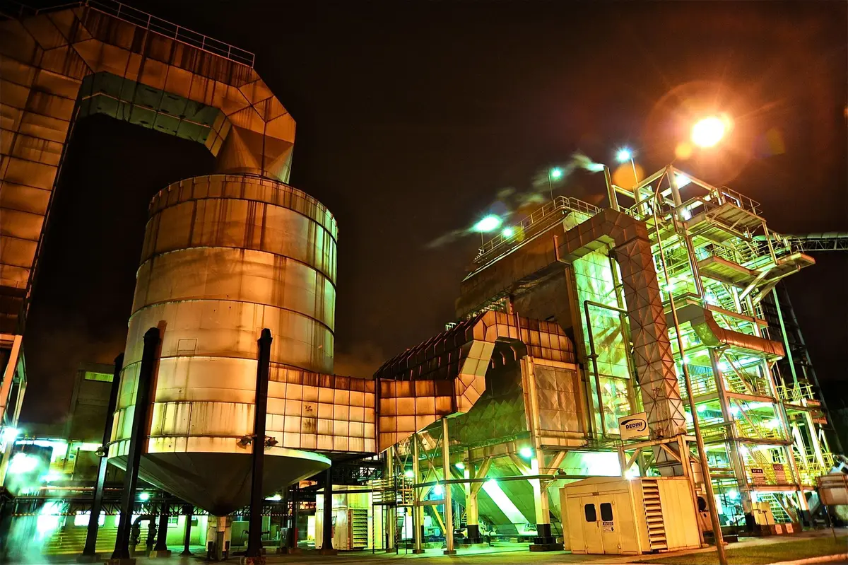 A computer rendering of the completed Terafab facility at sunset, gleaming metal and glass surfaces reflecting warm light, geometric architectural forms suggesting industrial precision, the structure dominating an empty landscape, a sense of scale and futuristic ambition