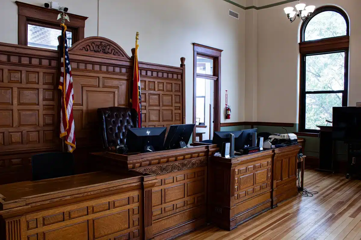 Courthouse hallway with empty benches, harsh overhead lighting casting long shadows, a single attorney's briefcase on a bench
