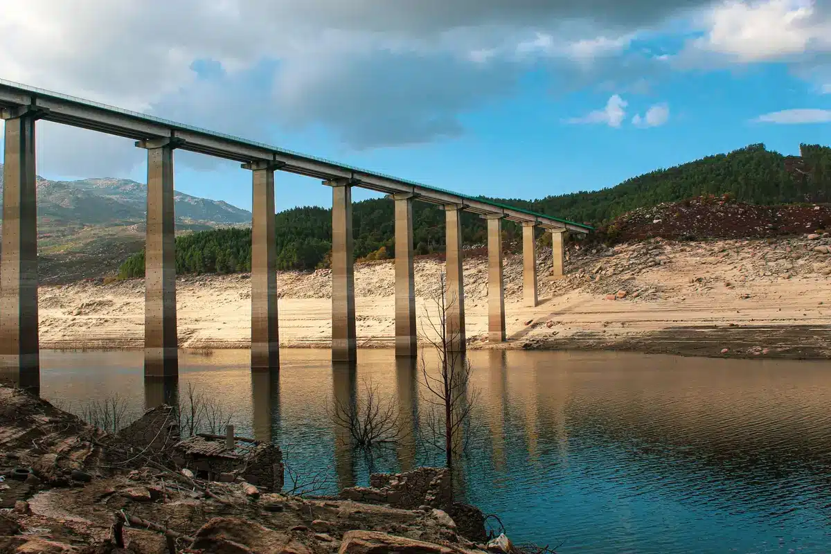 A shallow European river with exposed sandbars and rocky outcrops, ships stranded or navigating carefully through narrow passages, heatwaves shimmering above the water surface.