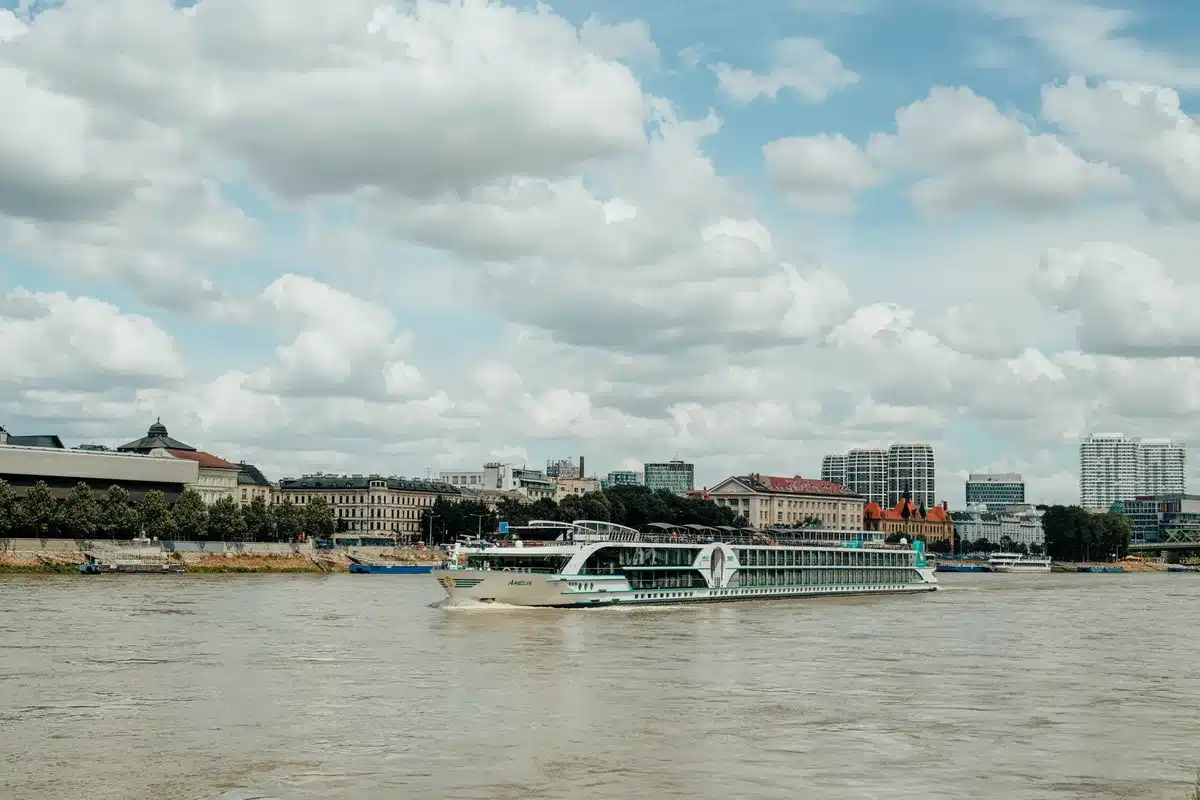 A tour bus on a European riverside road, passengers boarding or inside, replacing what would have been a river segment of their cruise, late afternoon light.