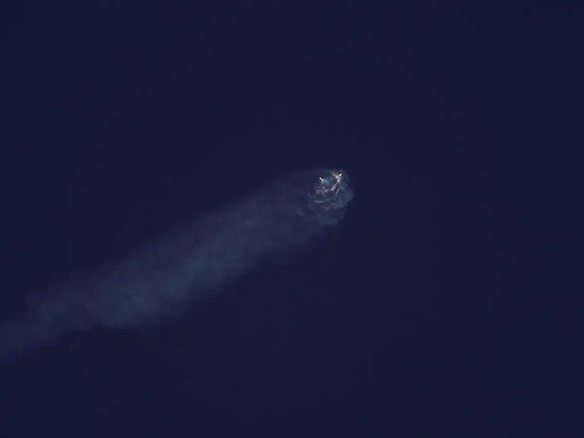 A Falcon 9 first stage booster ascending from a coastal launch complex at dawn, flame and exhaust illuminating the pre-dawn sky, the rocket's trajectory cutting through thin clouds above the Atlantic