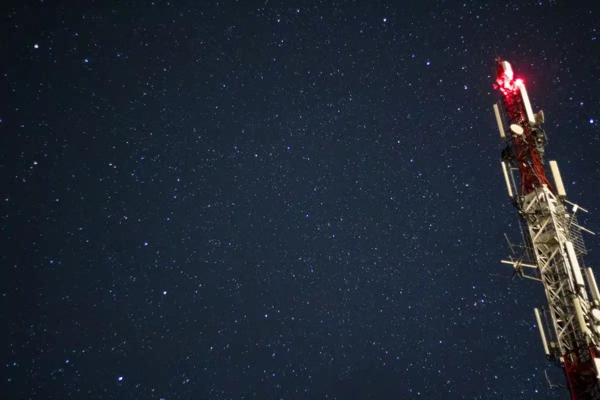 A night sky filled with streaks of light representing satellite orbital paths, a glowing Earth below, constellation patterns visible above the horizon